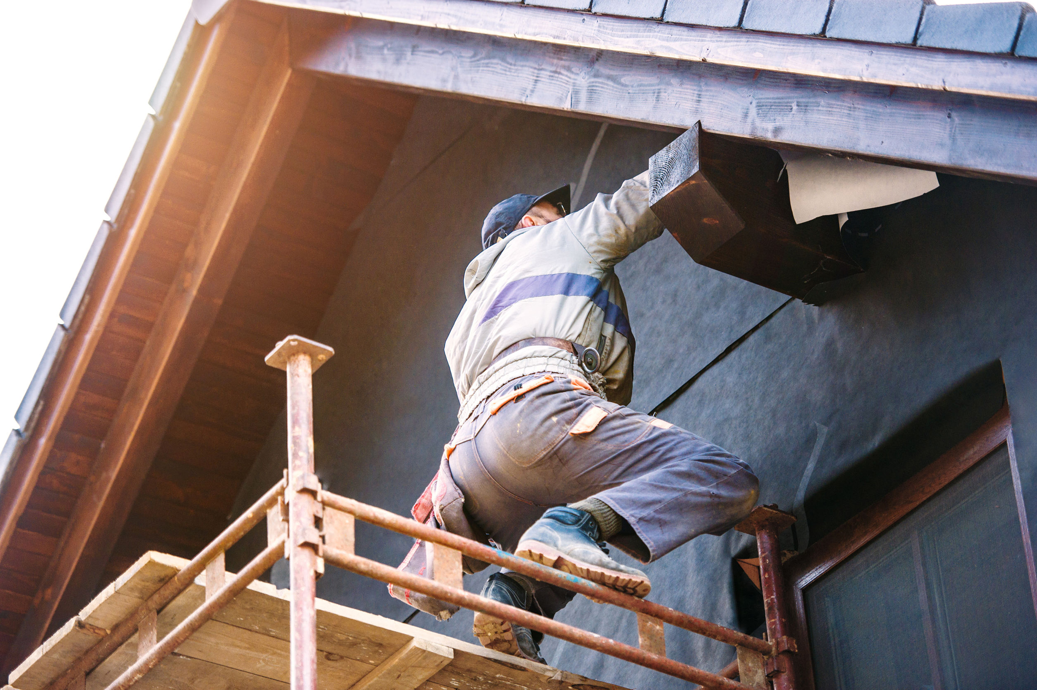 Construction worker thermally insulating house with glass wool and foil.